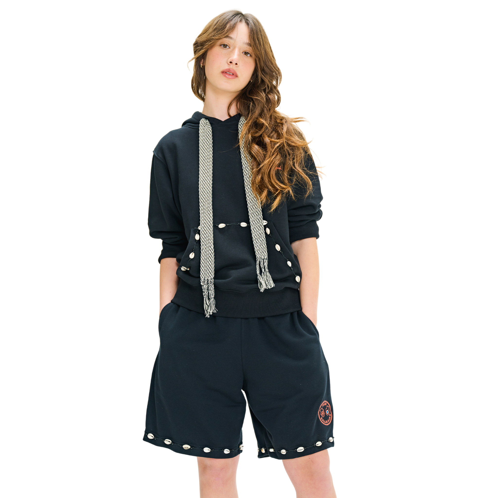 Front view of female model in long-sleeve hoodie with embroidered logo, handmade cowrie shells, and woven black-white straps