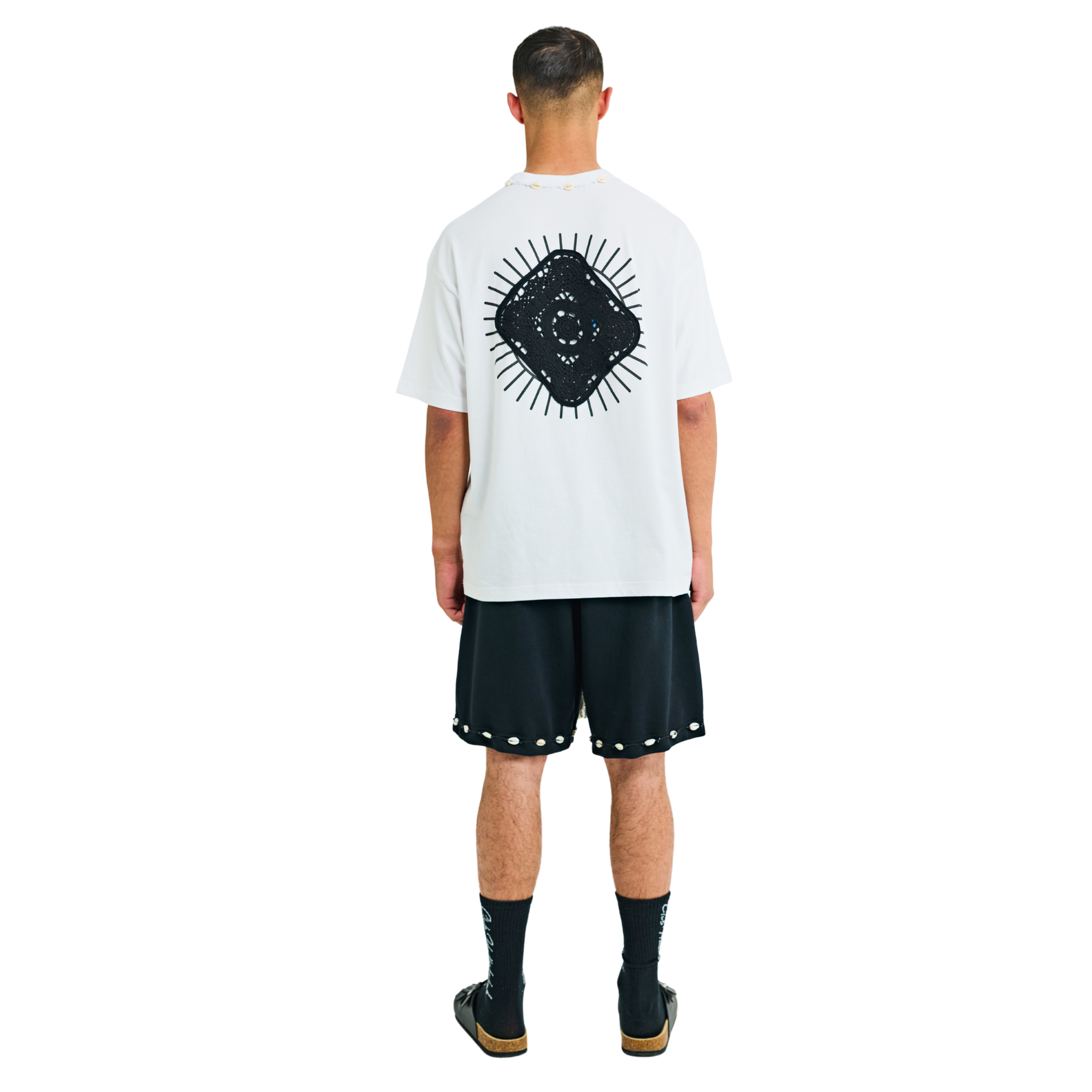 Model wearing white T-shirt, back view, showing black sunburst appliqué and cowrie shell neckline