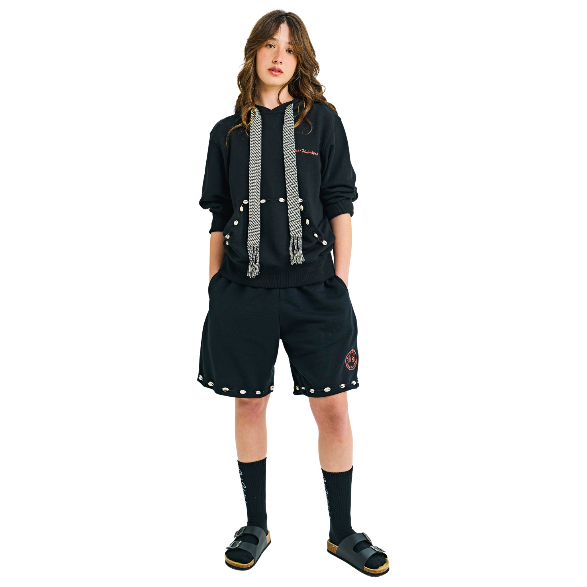 Front view of female model in unisex black shorts, braided drawstring, cowrie shell hem, 100% cotton, embroidered details