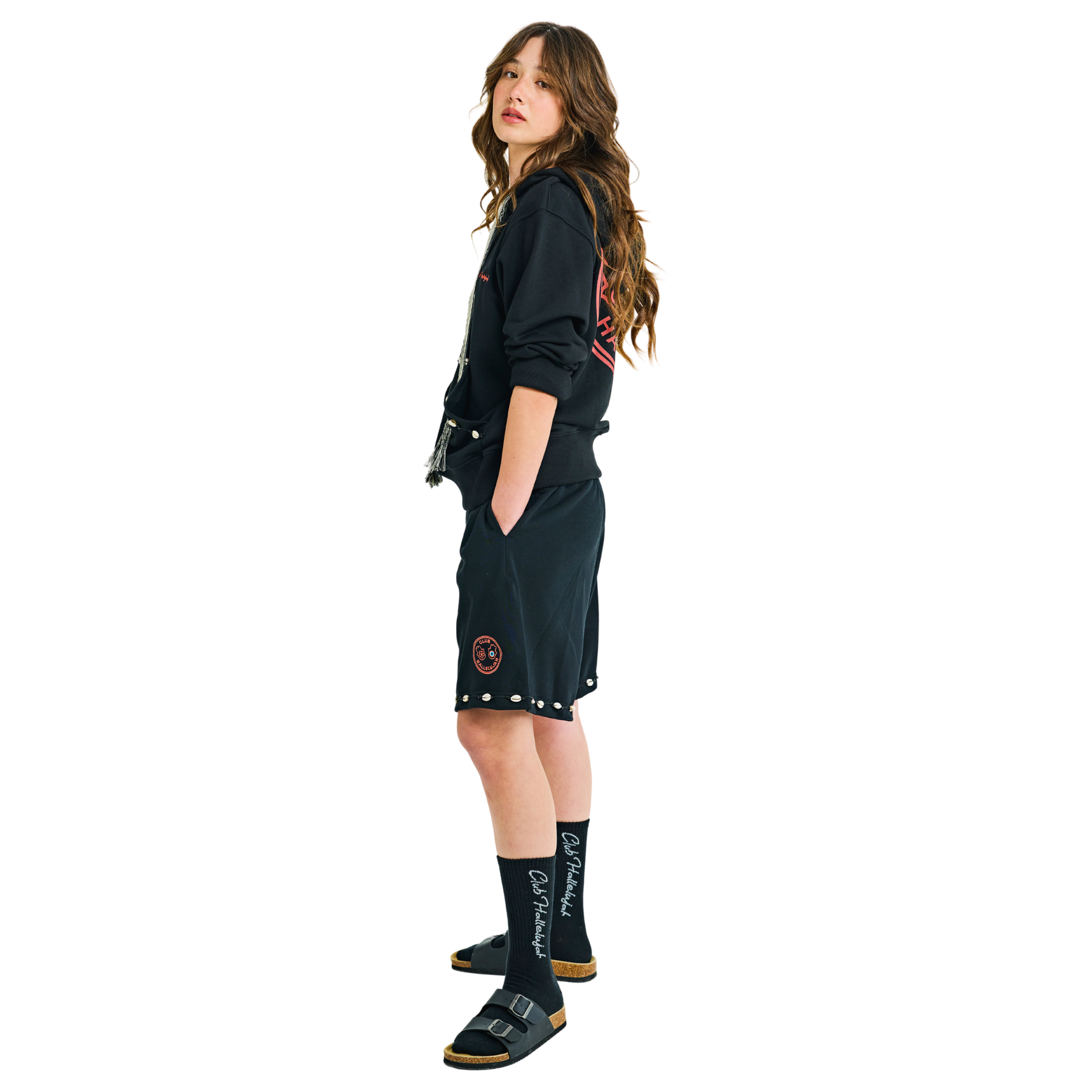 Side view of female model wearing embroidered long-sleeve hoodie with handmade cowrie shells and woven tassels