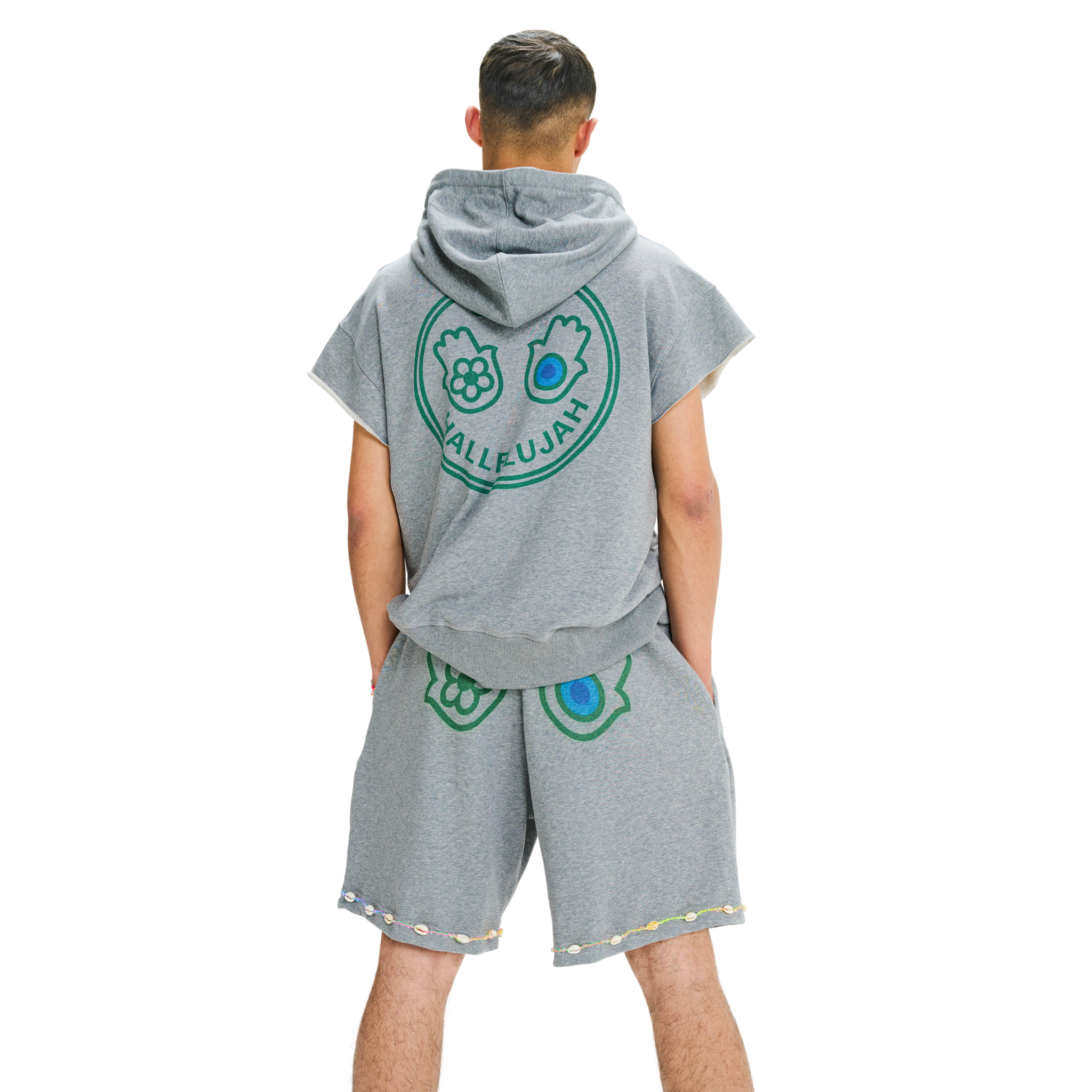 Back view of male model in unisex grey oversized shorts with printed hand symbols and cowrie shell embroidered hemline