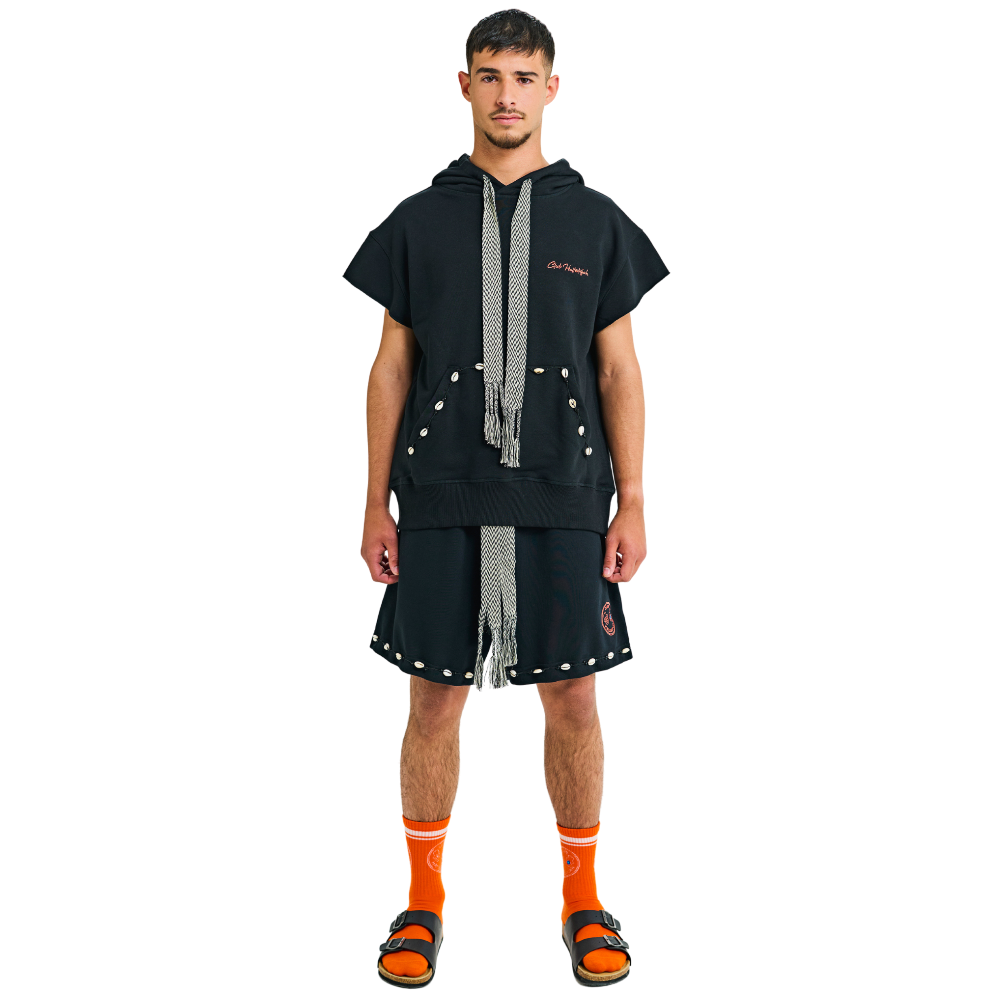 Front view of male model in unisex black shorts, braided drawstring, cowrie shell hem, 100% cotton, embroidered logo