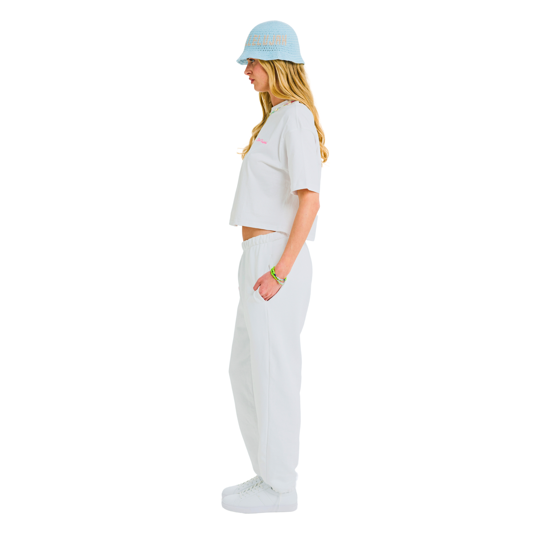 Model in white crop top, side view, showing pink 'Club Hallelujah' embroidery and cowrie shell neckline