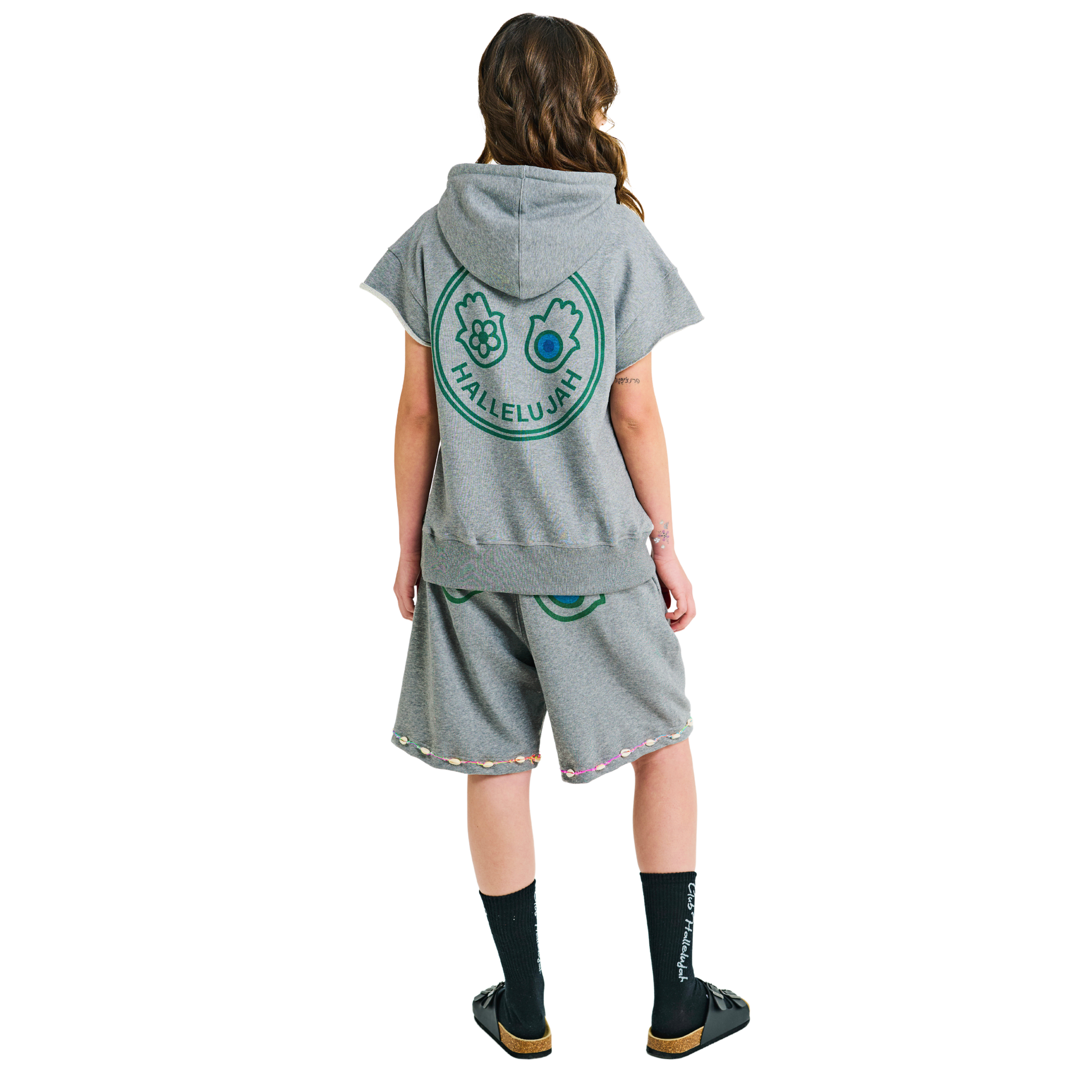 Back view of female model in unisex grey oversized shorts with printed hand symbols and cowrie shell embroidered hem