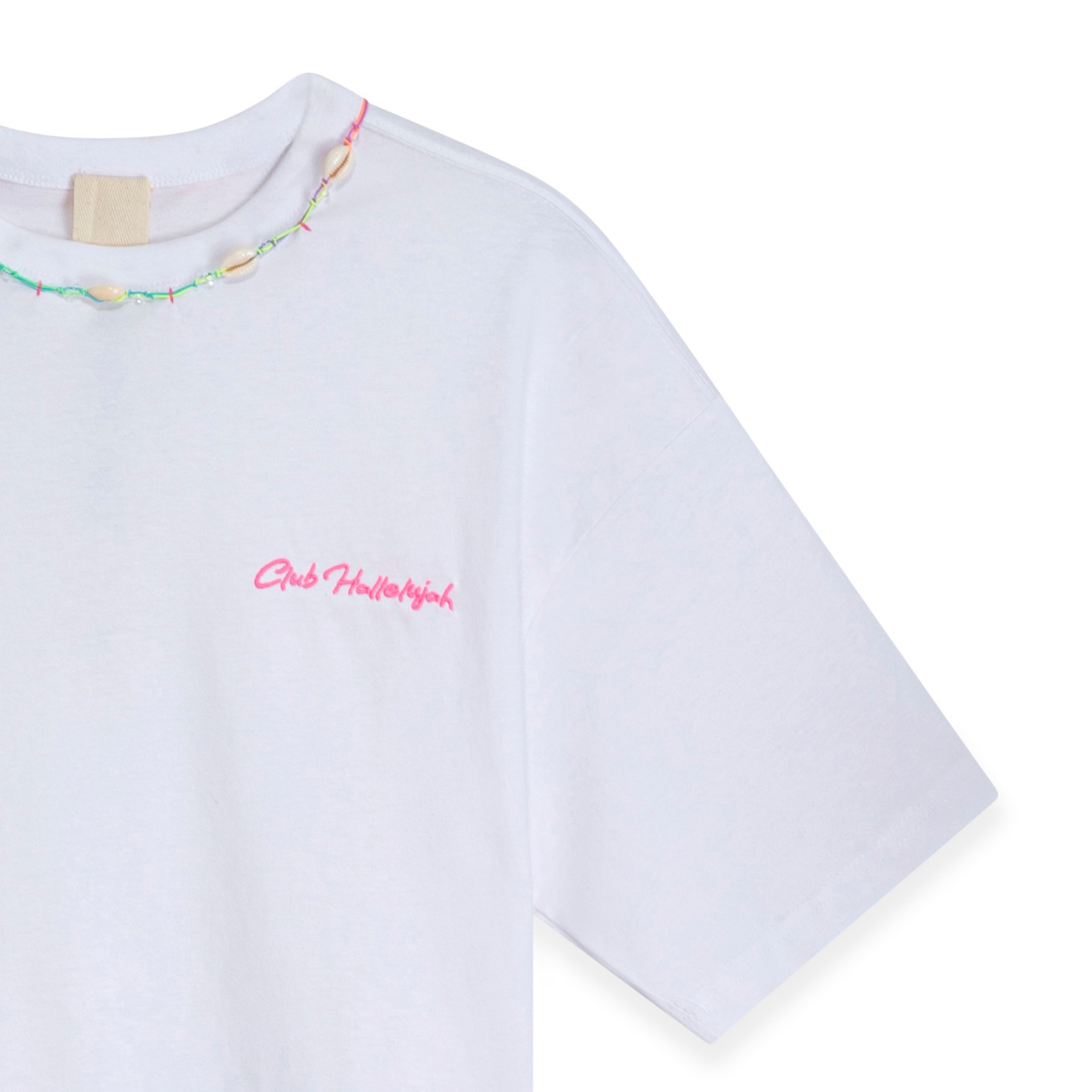 Close-up of white crop top with pink 'Club Hallelujah' embroidery and cowrie shell details at neckline