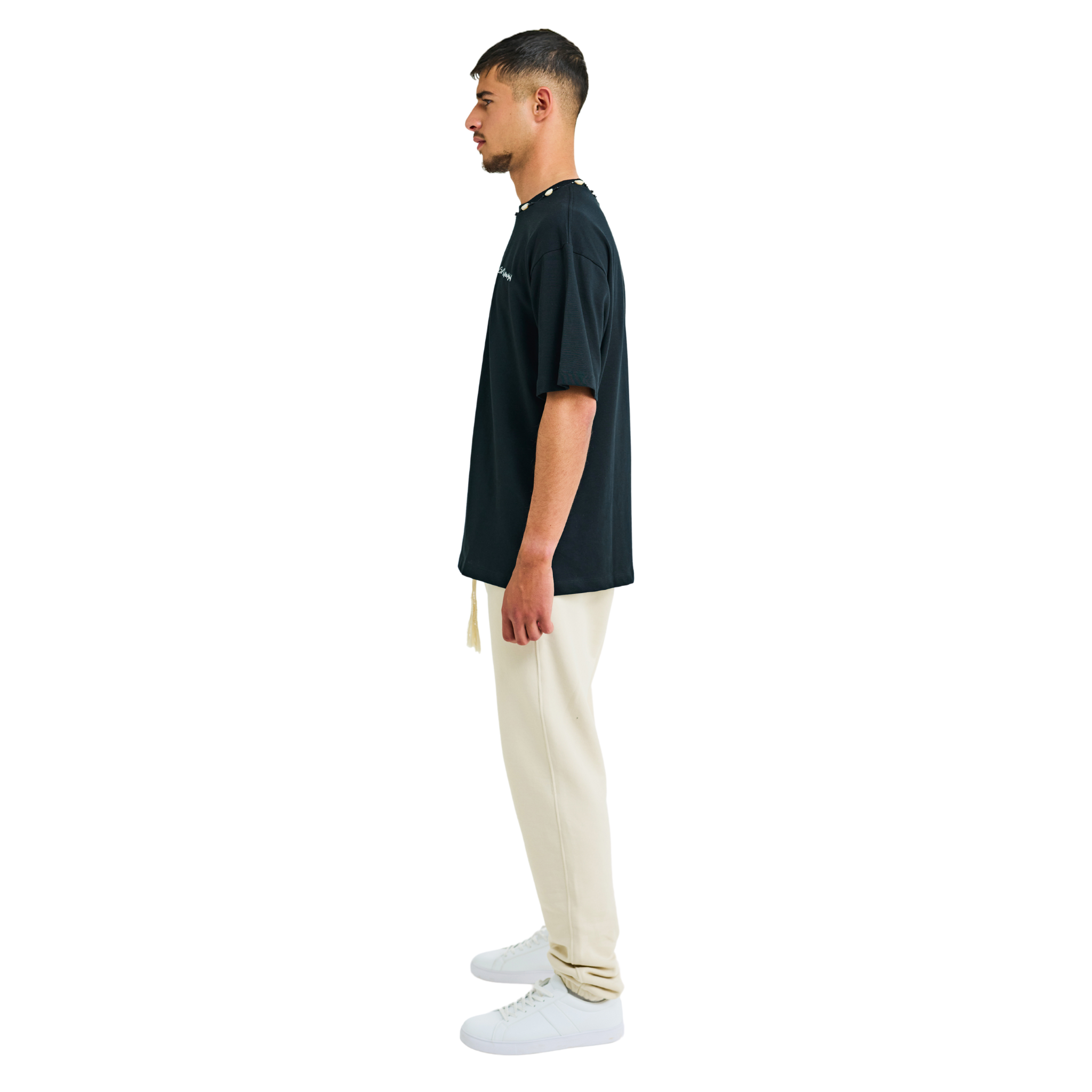 Side view of male model in unisex black oversized T-shirt with embroidered chest logo and handmade braided neckline