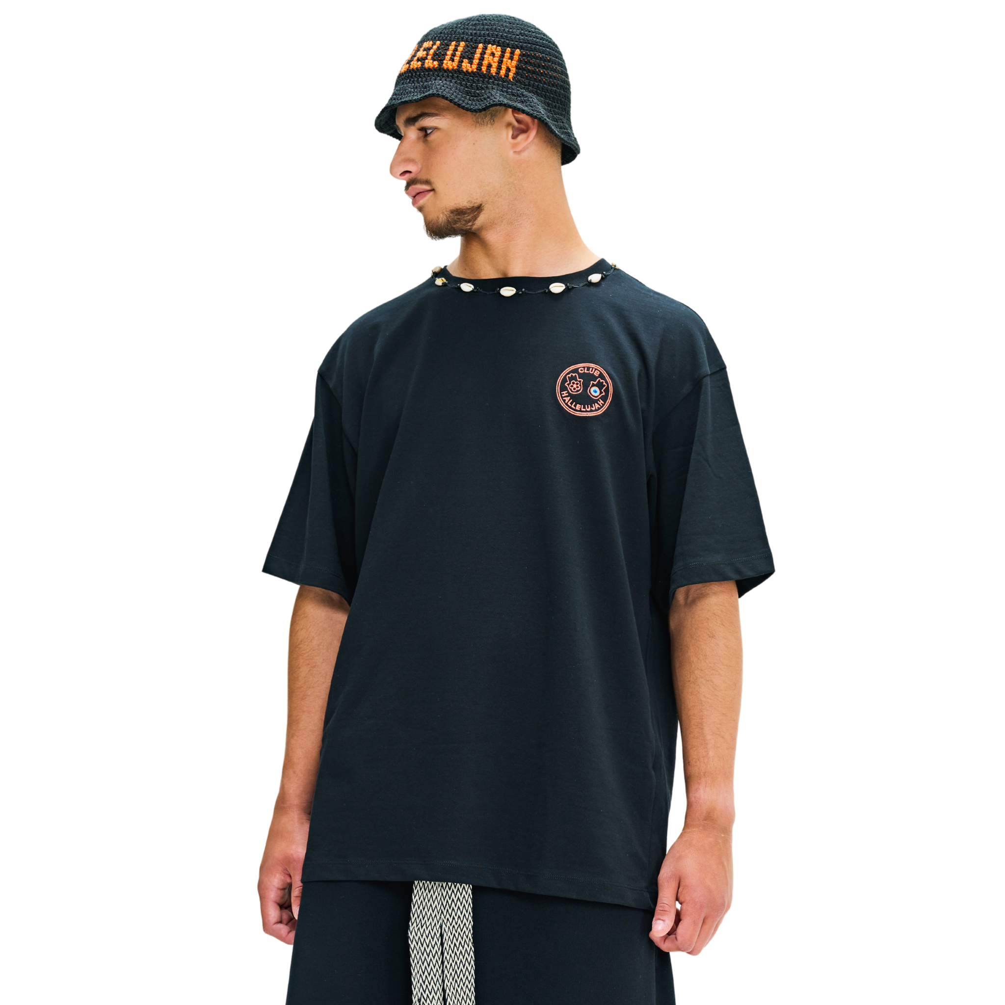 Male model wearing black oversized T-shirt, side view, showing cowrie shell neckline and hamsa back print