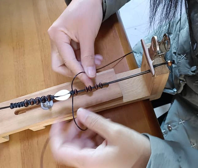 Close-up of artisan hands braiding a beaded cord on a wooden loom by Club Hallelujah, handmade fair trade craftsmanship