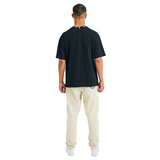 Back view of male model wearing unisex black oversized T-shirt with handmade braided neckline and relaxed fit