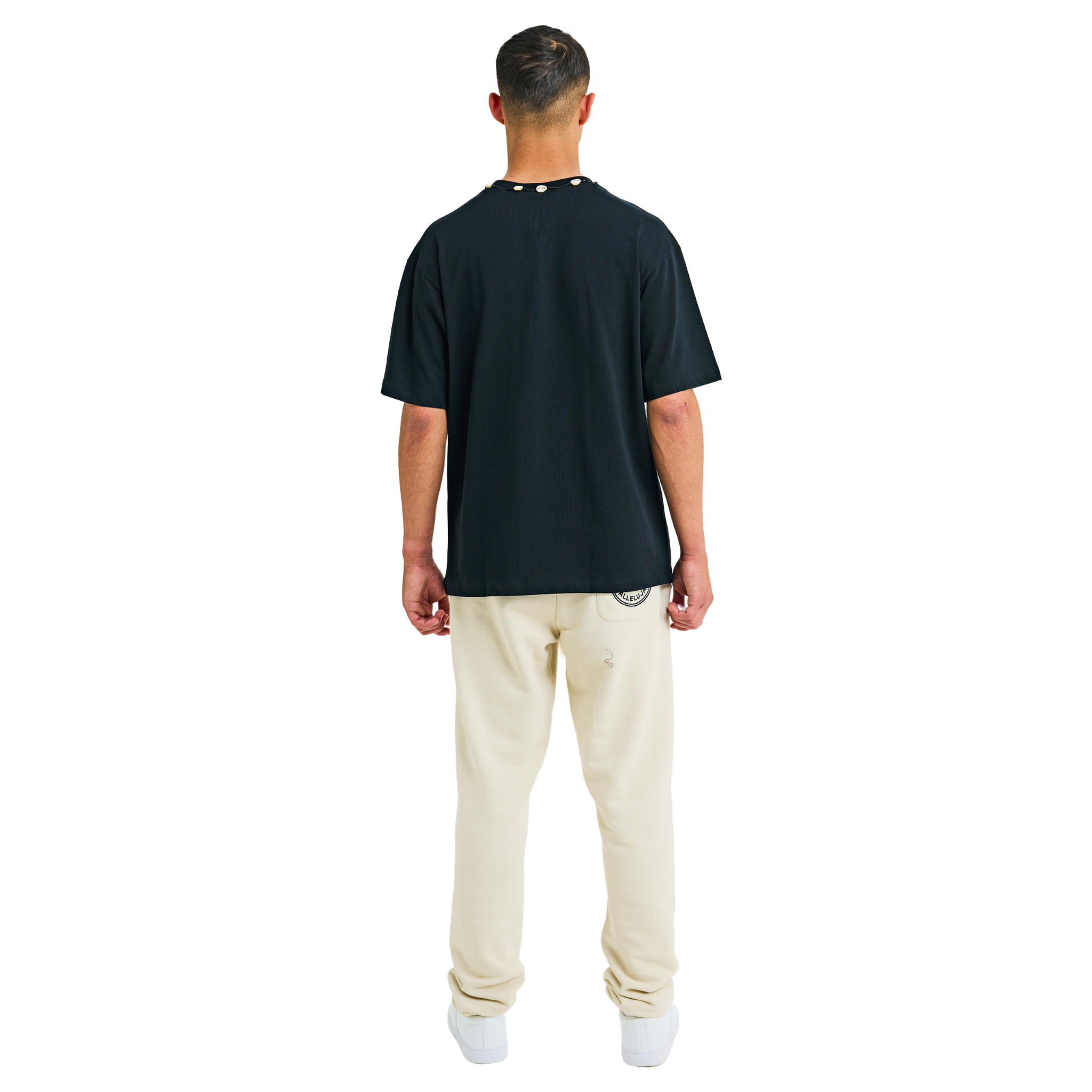 Back view of male model wearing unisex black oversized T-shirt with handmade braided neckline and relaxed fit