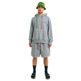 Front view of male model wearing unisex grey hoodie and shorts set with embroidered details, hand-woven drawstrings, and cowrie shell trims