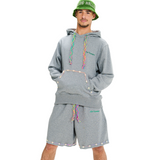 Front view of male model wearing unisex grey hoodie with embroidered kangaroo pocket and colorful hand-woven drawstring