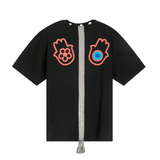 Black oversized cotton T-shirt, back view, with hamsa prints, woven strap with tassels, and cowrie shell details