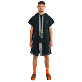 Front view of male model in unisex black shorts, braided drawstring, cowrie shell hem, 100% cotton, embroidered logo