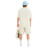Male model wearing unisex Sabbia T-shirt, showing back with sunburst Club Hallelujah lace logo, handmade cowrie shells, 100% cotton.