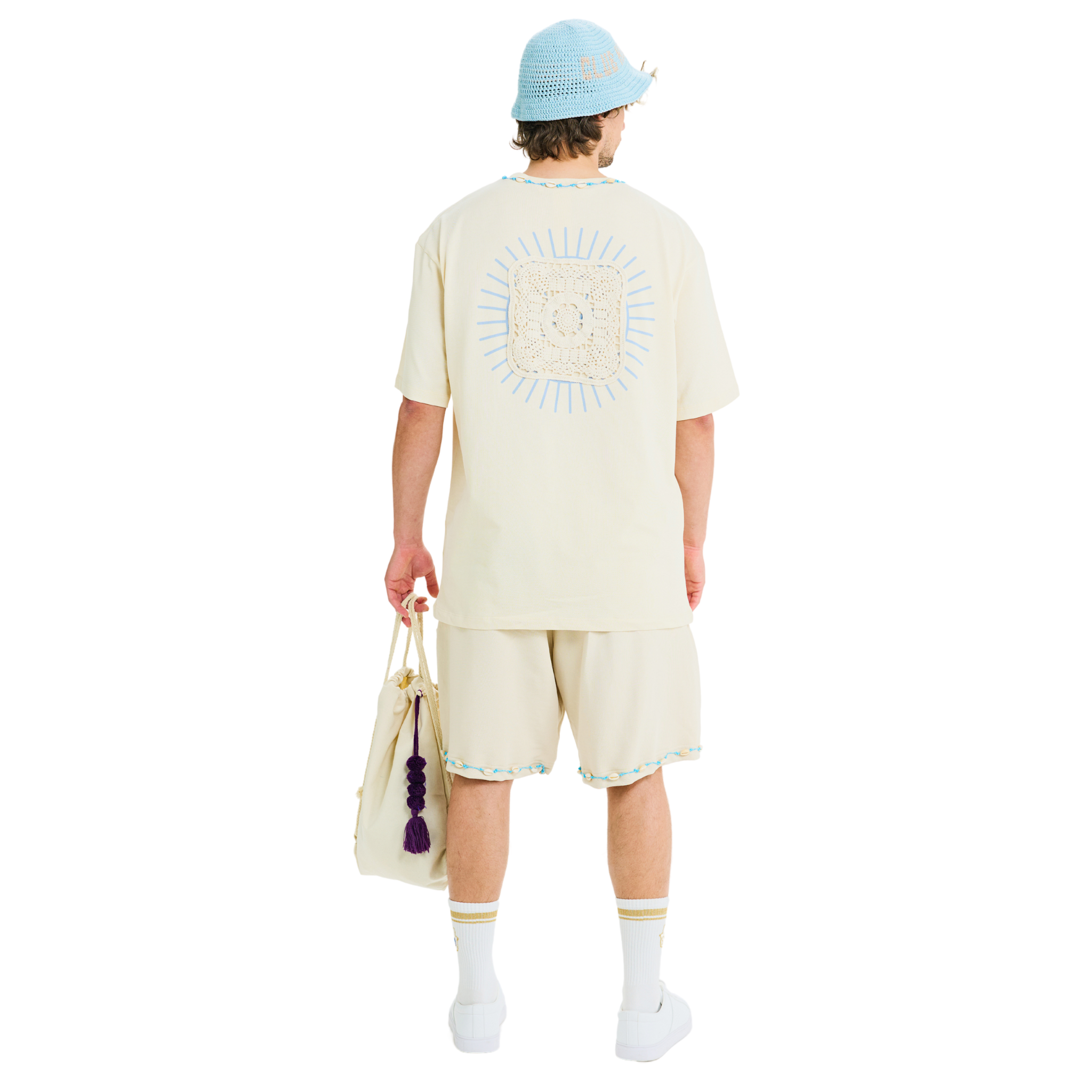 Male model wearing unisex Sabbia T-shirt, showing back with sunburst Club Hallelujah lace logo, handmade cowrie shells, 100% cotton.