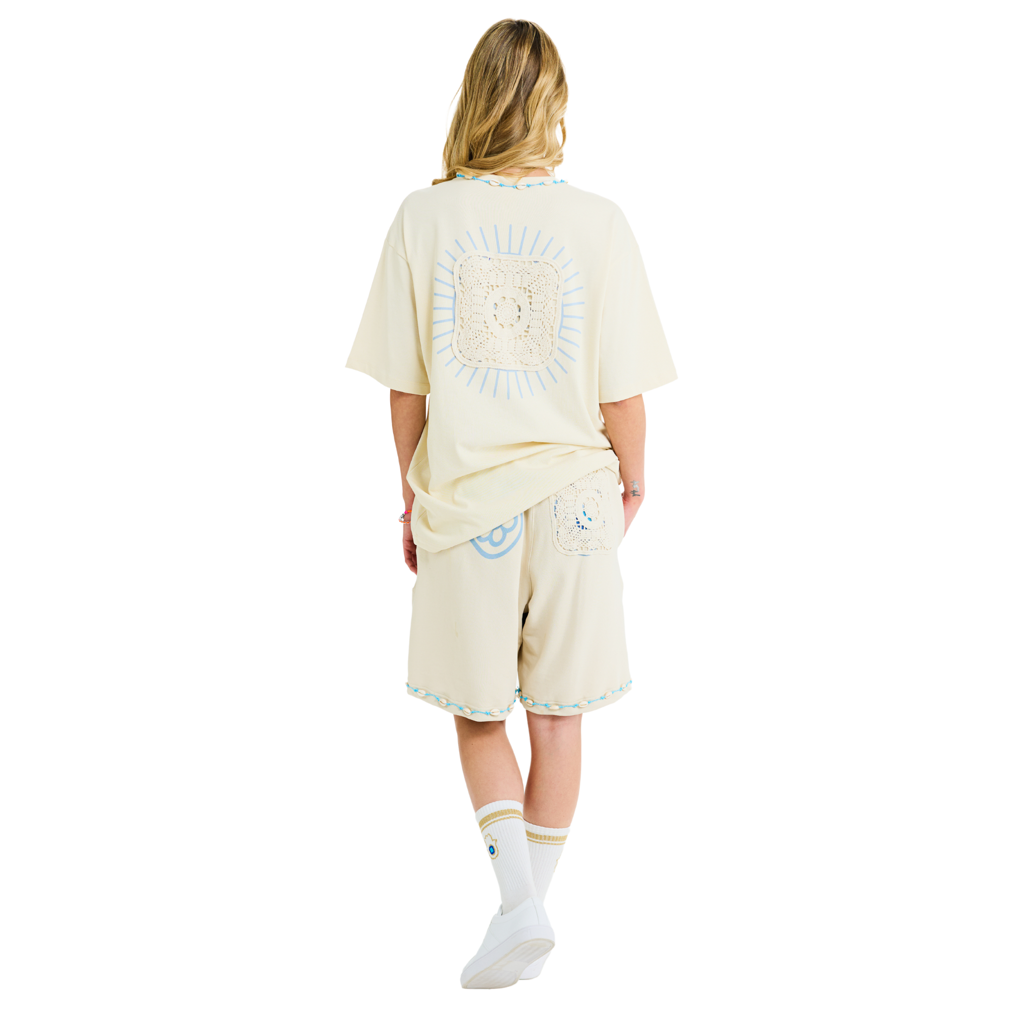 Female model showing back of unisex Sabbia T-shirt with Club Hallelujah sunburst lace logo, handmade cowrie shell details, 100% cotton