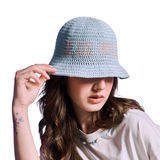 Model wearing baby blue crocheted bucket hat with orange 'CLUB HALLELUJAH' text, side view