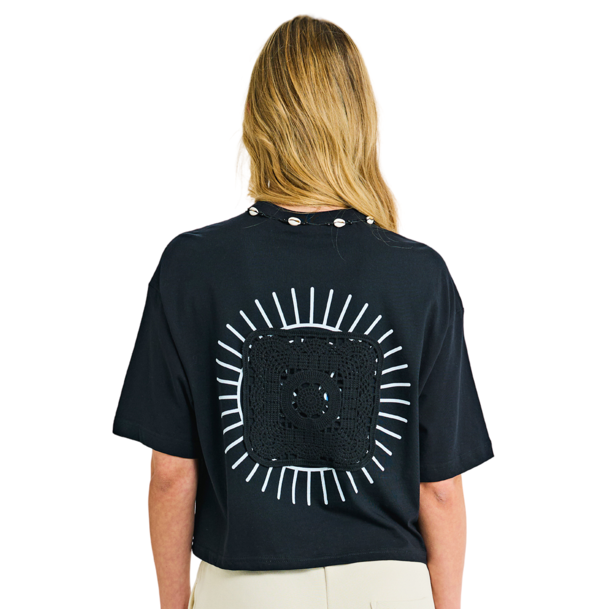 Model wearing black crop top, back view, showing sunburst appliqué and cowrie shell neckline