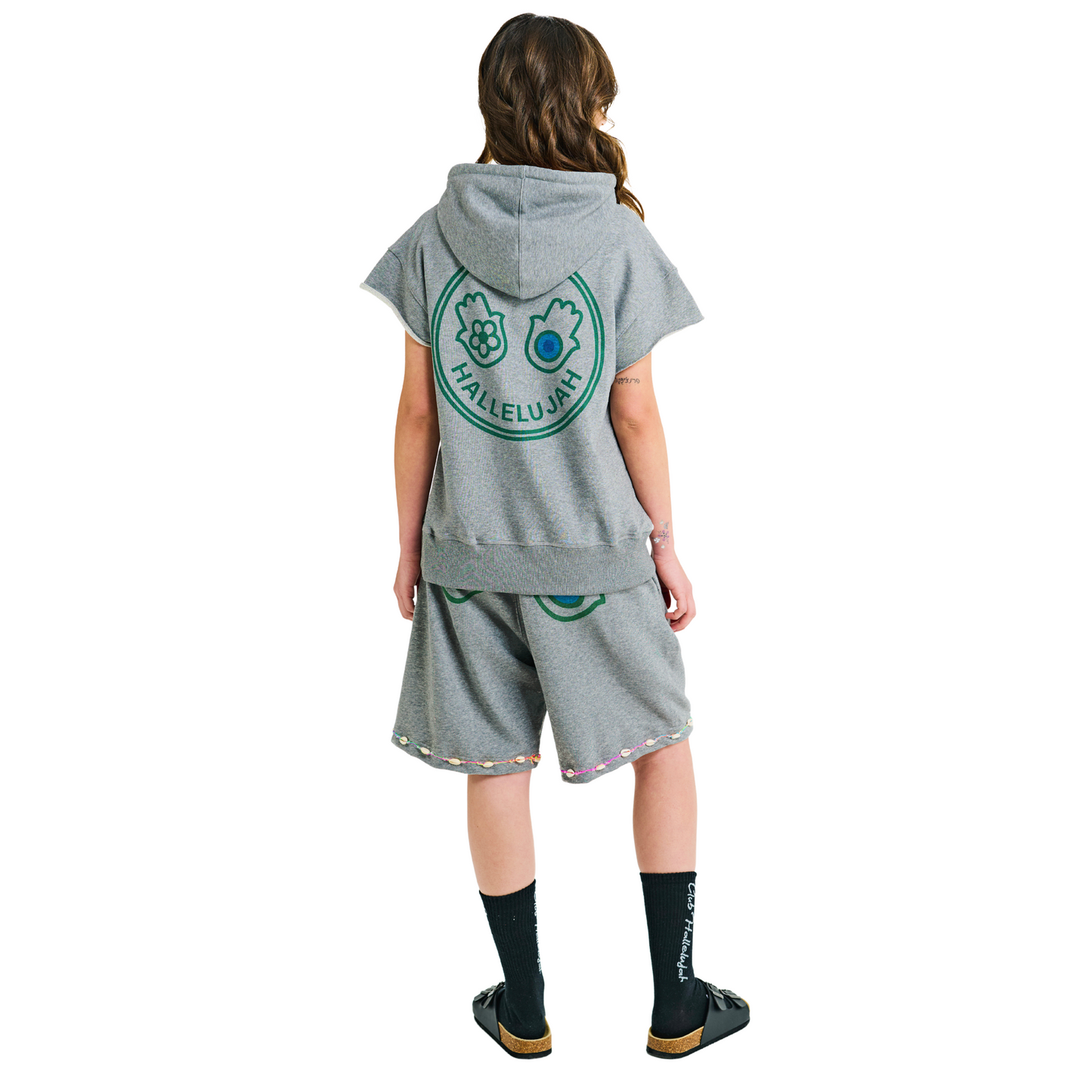 Back view of female model in unisex grey oversized shorts with printed hand symbols and cowrie shell embroidered hem