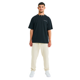 Front view of male model in unisex black oversized T-shirt with embroidered logo and handmade braided neckline