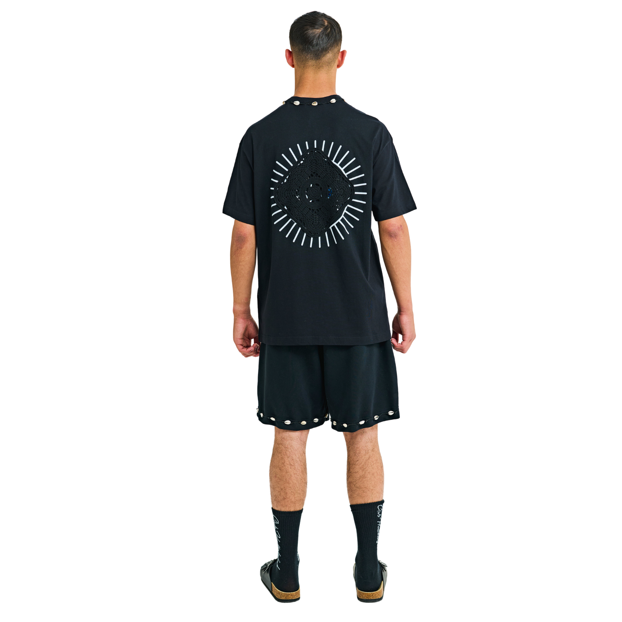 Model wearing black T-shirt, back view, showing sunburst appliqué and cowrie shell neckline